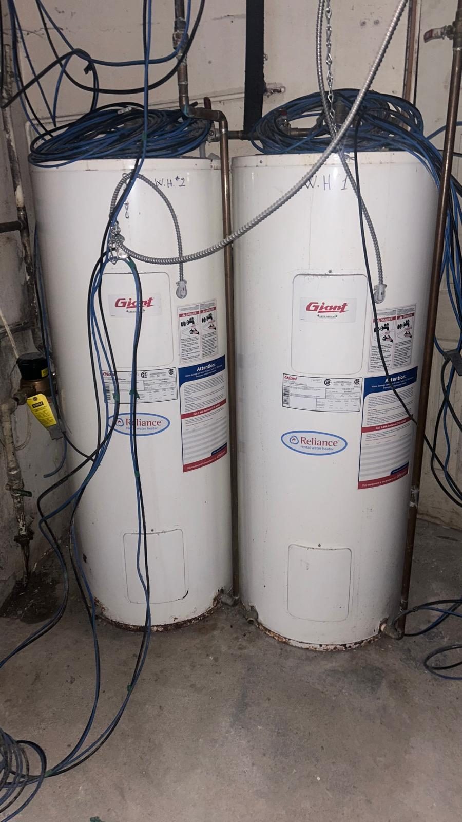 Two rental domestic hot water tanks labelled WH-1 and WH-2 in the building's mechanical space, with surface corrosion at the base